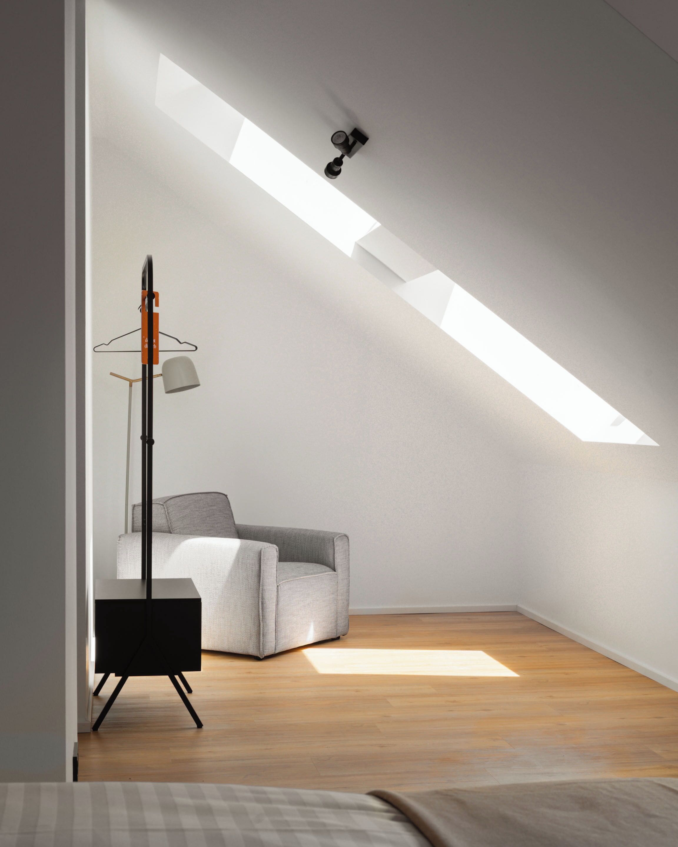 A modern, minimalist room with a sloped ceiling, a grey armchair, a floor lamp, and a small table.
