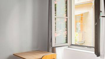 A small room with a wooden desk, a chair, a bed, and a window with curtains.