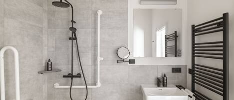 A modern bathroom with a shower, sink, and towel rack.