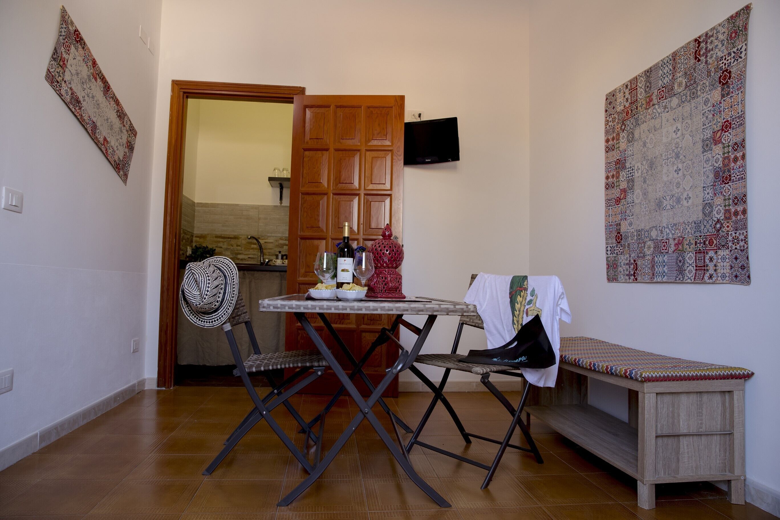 Un espace de vie compact comprenant une table à manger, deux chaises, un banc et un téléviseur fixé au mur.