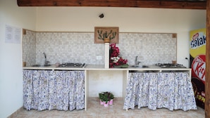 A kitchen with two sinks, a wooden ceiling, tiled backsplash, and patterned curtains. - Villa I 2 Pini (San Vito Lo Capo)