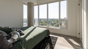 A bedroom with a large window, a bed, a lamp, and a view of a cityscape. - Executive 2BD+Wifi+Parking+EV (Kitchener)