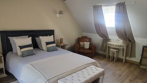 Une chambre avec un grand lit, un banc en bois, une petite table et une chaise.