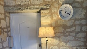 Une pièce comprenant deux fauteuils en osier avec des coussins verts, un lampadaire et une horloge murale.