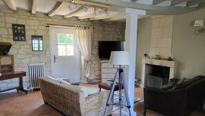 Un salon spacieux avec un mur en pierre, une cheminée, un téléviseur et une grande fenêtre agrémentée de rideaux.