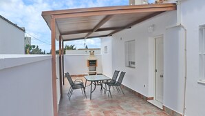 A covered patio with a table and chairs, a grill, and a door.
