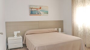 A bedroom with a bed, a nightstand, a lamp, a power outlet, and a painting of a surfboard on a car.