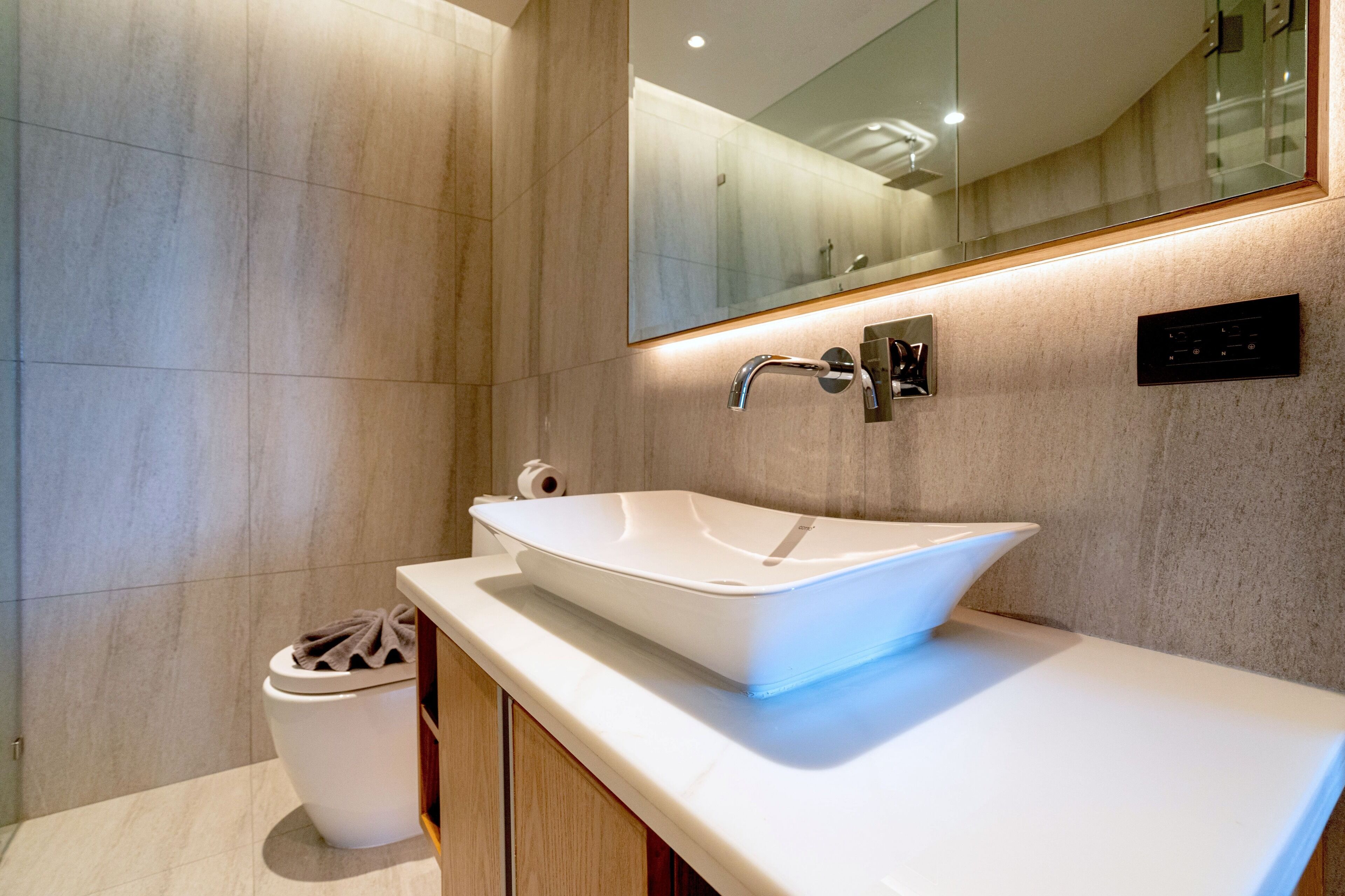A modern bathroom with a white vessel sink, a mirror above it, and a toilet to the left.