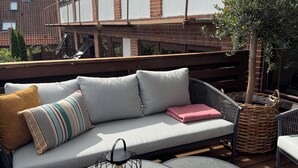 A rooftop terrace with a sofa, two round tables, and a wicker basket. - Hotel Arnkilhus (Sønderborg)