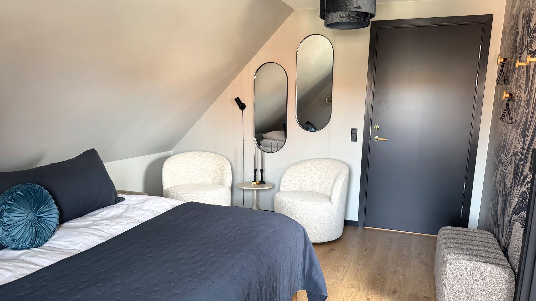A bedroom with a bed, two chairs, a small table, a door, and a mirror.