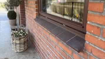 A brick building with a window, a potted plant, and a wicker basket.
