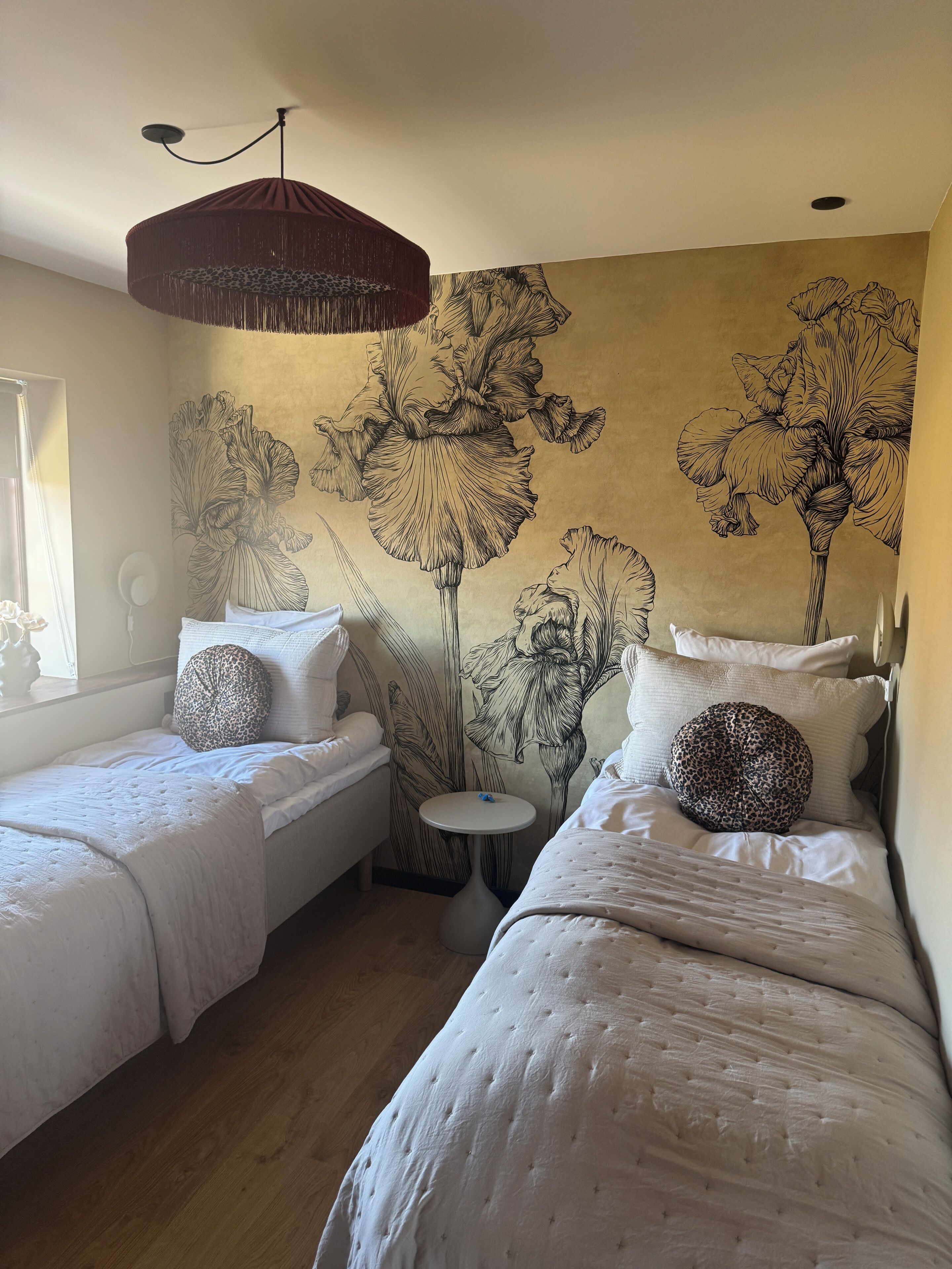 Un dormitorio con dos camas individuales, una mesita redonda pequeña y un gran mural de flores en la pared.