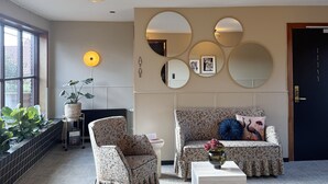 A living room with a sofa, two armchairs, a coffee table, a fireplace, and wall-mounted mirrors. - Hotel Arnkilhus (Sønderborg)