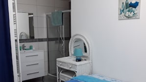 A bedroom with a bed, a white wicker vanity with a mirror, a blue lamp, and a bathroom visible in the background. - Rental House St Hilaire De Riez 6/8 people 300 m from the beach, 2 stars (Saint-Hilaire-de-Riez)