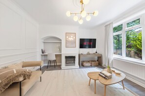 A living room with a beige sofa, a coffee table, a fireplace, a TV, and a large window with a view of greenery.