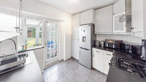 A modern kitchen with white cabinets, a built-in oven, a stove, and a window with a view of the garden. - Modern 2-Bedroom Home in Bromley (Bromley)