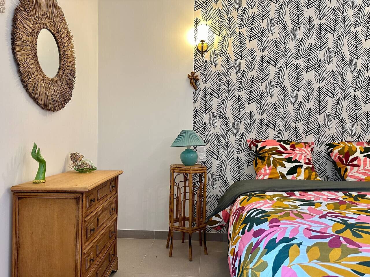 A bedroom with a bed, a dresser, a mirror, a lamp, and patterned wallpaper.