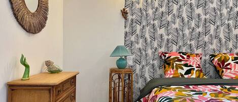A bedroom with a bed, a dresser, a mirror, a lamp, and patterned wallpaper.