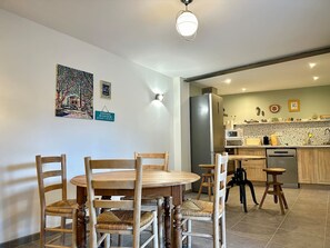 Un comedor con una mesa redonda de madera y sillas, una cocina con refrigerador y microondas, y un piso de baldosas.
