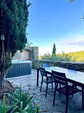 An outdoor patio with stone flooring, a wooden table and chairs, a stone wall, and a hot tub.