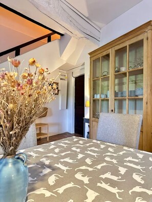 A dining area with a table covered by a patterned tablecloth, a vase with dried flowers, and a wooden cabinet with glass doors.