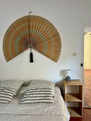 A bed with striped bedding, a wall-mounted fan, and a bedside table with a lamp.