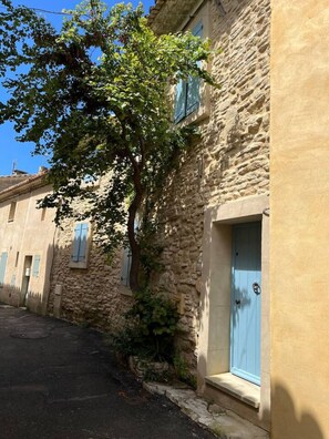 A narrow street with stone buildings, one with a blue door and shutters.