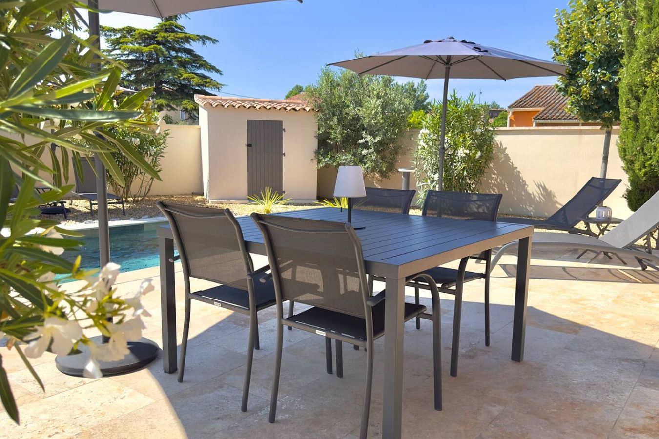 Een terras buiten met een tafel, stoelen, een zwembad en een lamp.