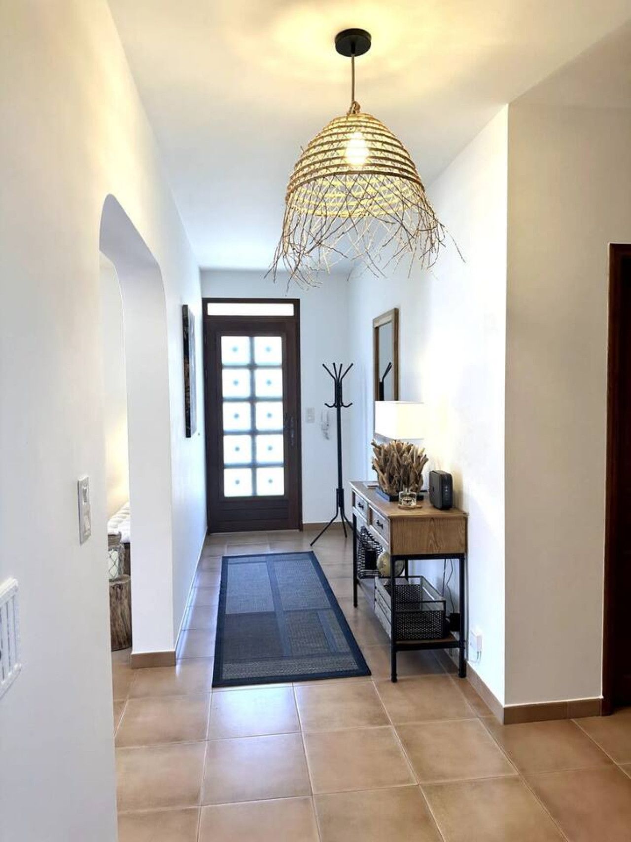 A hallway with a modern light fixture, a door with a grid pattern, a small table with a lamp, and a rug.