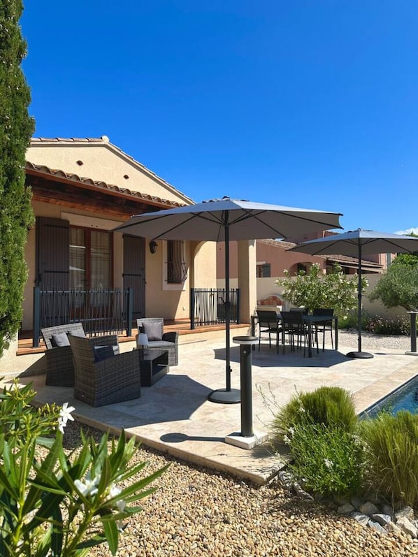 Une terrasse avec des meubles d’extérieur, des parasols et une piscine.