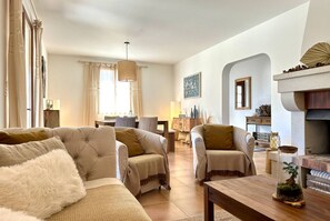 Un salon comprenant un canapé, des fauteuils, une table basse en bois, une cheminée et une lampe.