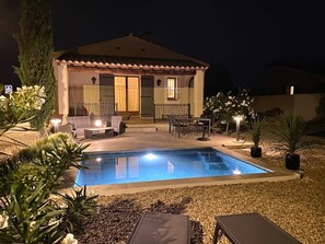 Une maison avec une piscine, un espace extérieur aménagé pour s’asseoir et une terrasse bien éclairée.