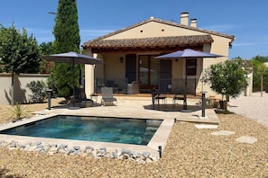 Une maison avec une piscine, du mobilier de jardin et une pergola dotée de parasols.