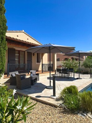 Une terrasse avec des meubles d’extérieur, des parasols et une piscine.