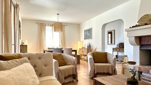 A living room with a sofa, armchairs, a wooden coffee table, a fireplace, and a lamp. - Les Lauriers Blancs, air-conditioned villa with swimming pool (L'Isle-sur-la-Sorgue)