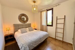 Een slaapkamer met een bed, nachtlampen, een spiegel, een raam met gordijnen en een houten ladder.
