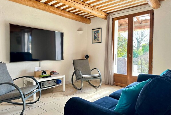 A living room with a flat-screen TV, two rocking chairs, a blue sofa, and a sliding glass door leading to an outdoor area.