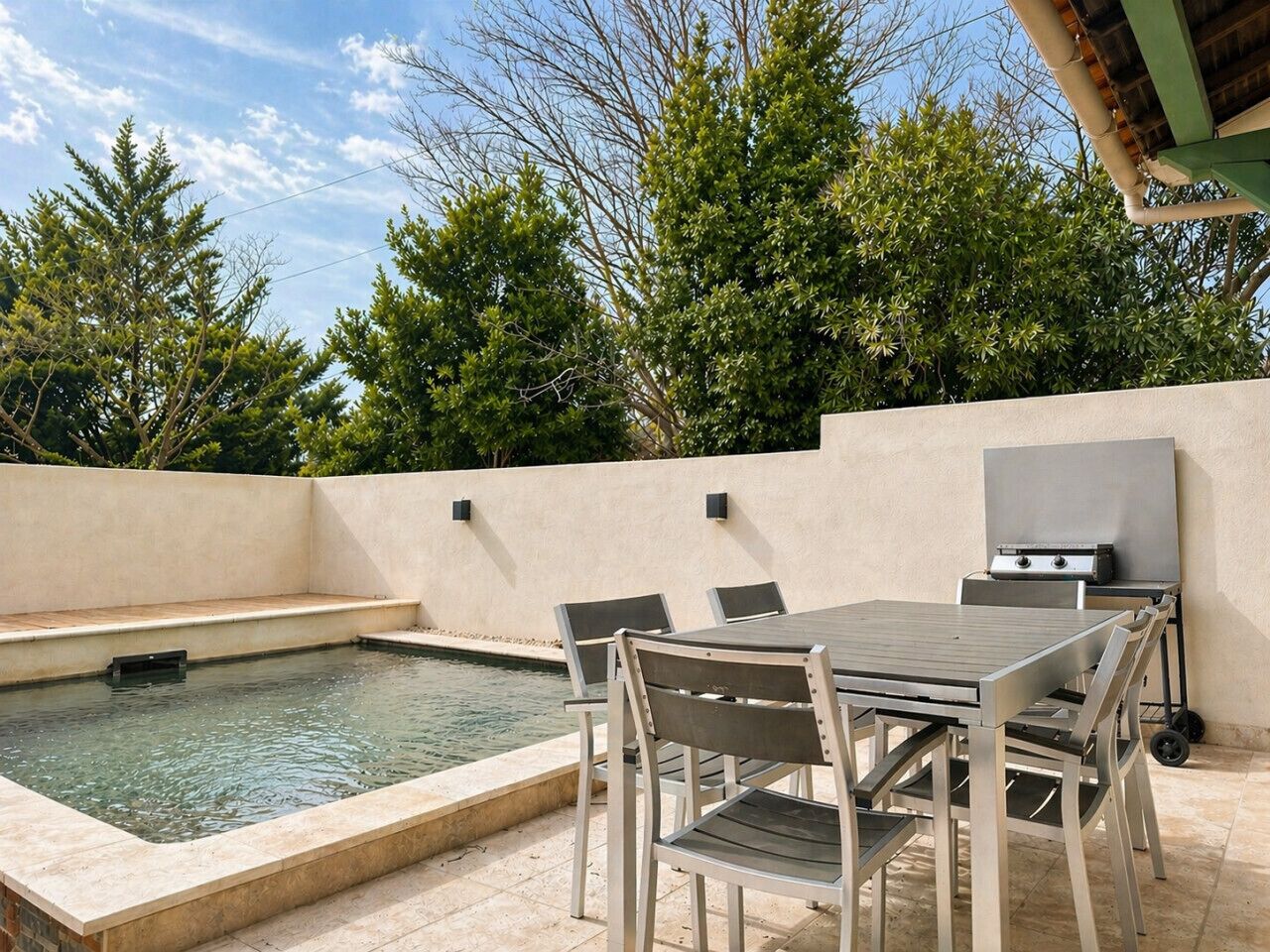A swimming pool with a table and chairs, a grill, and a pergola.