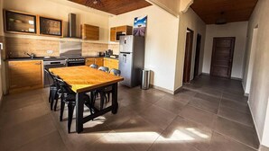 A modern kitchen with a wooden table and chairs, a refrigerator, and a microwave. - Villa Keromate, air-conditioned villa with natural pool. (Entraigues-sur-la-Sorgue)