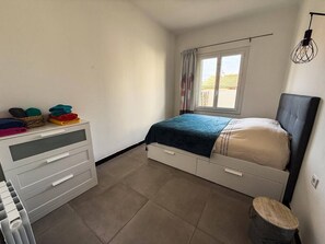 Et soveværelse med seng, kommode, et vindue med gardiner og en radiator.