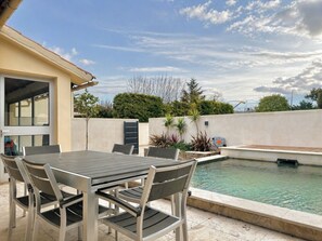 En udendørs terrasse med en pool, et bord med stole og en bygning med en dør.