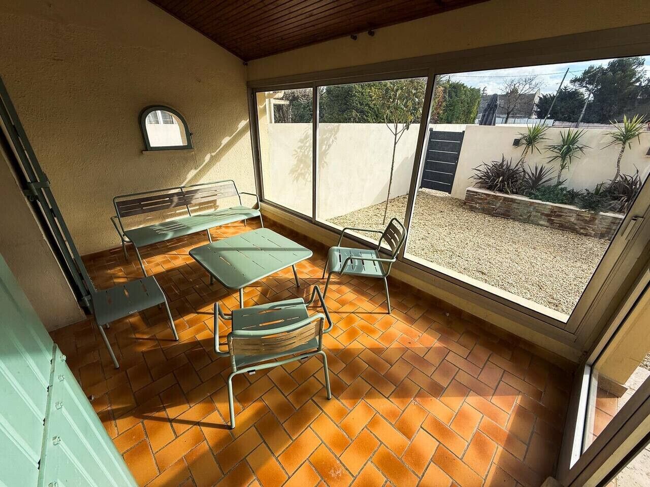 A patio with a table and chairs, a small window, and a view of a garden.