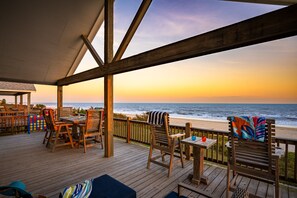 A wooden deck with outdoor seating, overlooking a beach at sunset. - Beachfront w/ Modern Interior, Swim Spa, Yard Games & Fire Pit (Gilchrist)