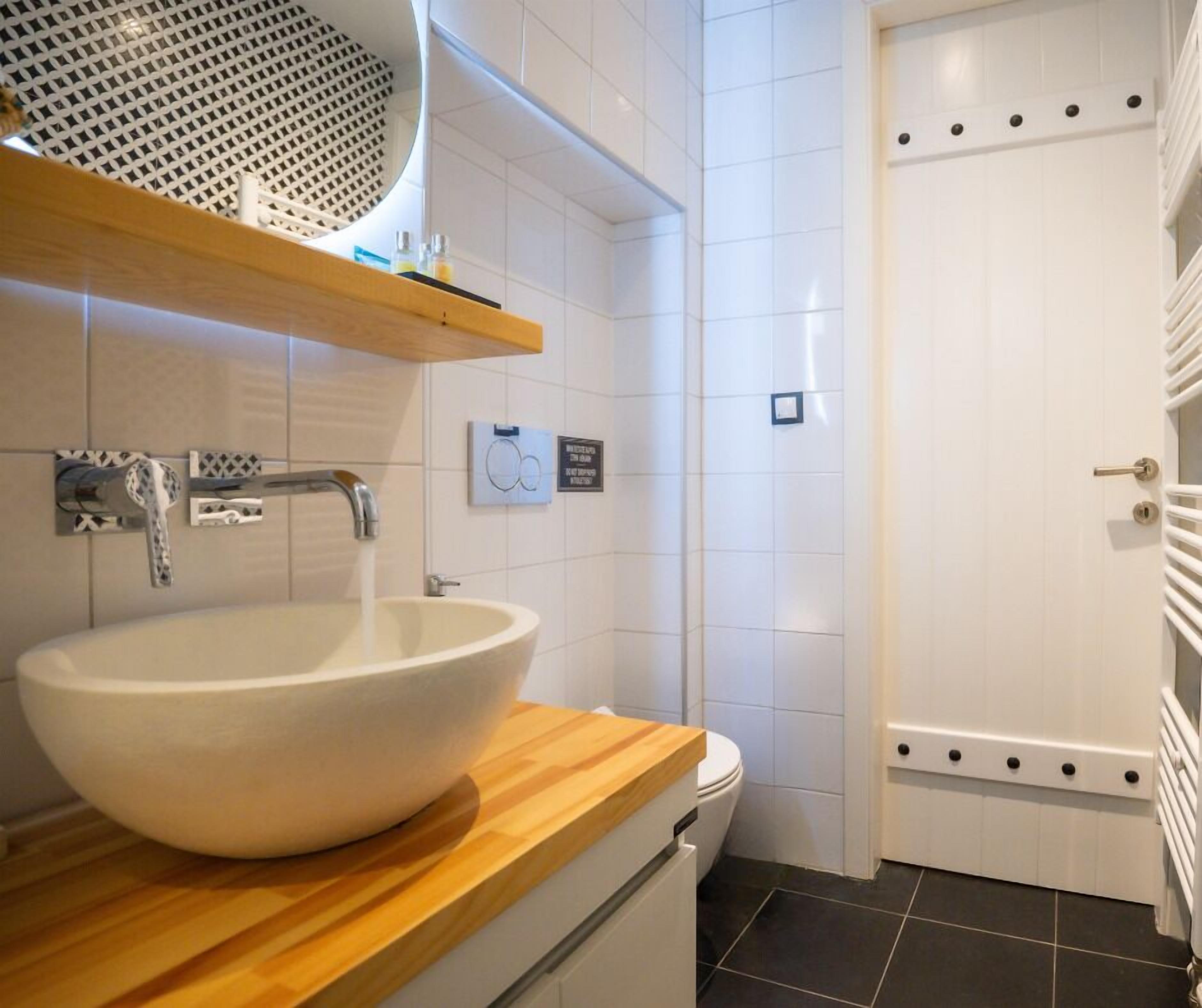 A bathroom with a large white sink, wooden countertop, and a white door with a towel rack.