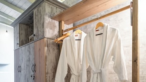 A wooden bench with two white bathrobes hanging on a rack, a wooden cabinet, and a basket on the floor. - Vayas Residences Legacy (Trikala)