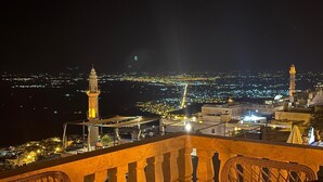 Vista nocturna desde un balcón con vistas a un paisaje urbano de edificios iluminados y dos imponentes minaretes.