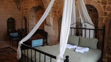 Una habitación de paredes de piedra con una cama con dosel, una silla de madera y una mesita.