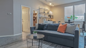 A modern living room with a grey sofa, a small round table, and a shelving unit above the sofa.
