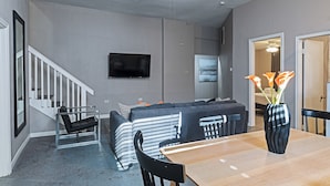 A modern living room with a sofa, a dining table, and a TV mounted on the wall.