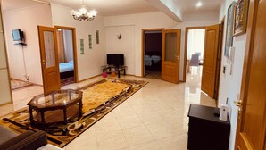 Een ruime woonkamer met een groot vloerkleed, een glazen salontafel en een televisie.